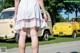 A woman in a white dress standing in front of a yellow car.