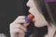 A woman with blue nails holding a red lollipop in her mouth.