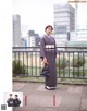 A woman in a kimono standing on a balcony with a handbag.