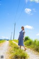 A woman in a blue and white dress standing on a dirt road.