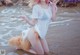 A woman in a white shirt and orange bikini sitting in the water.